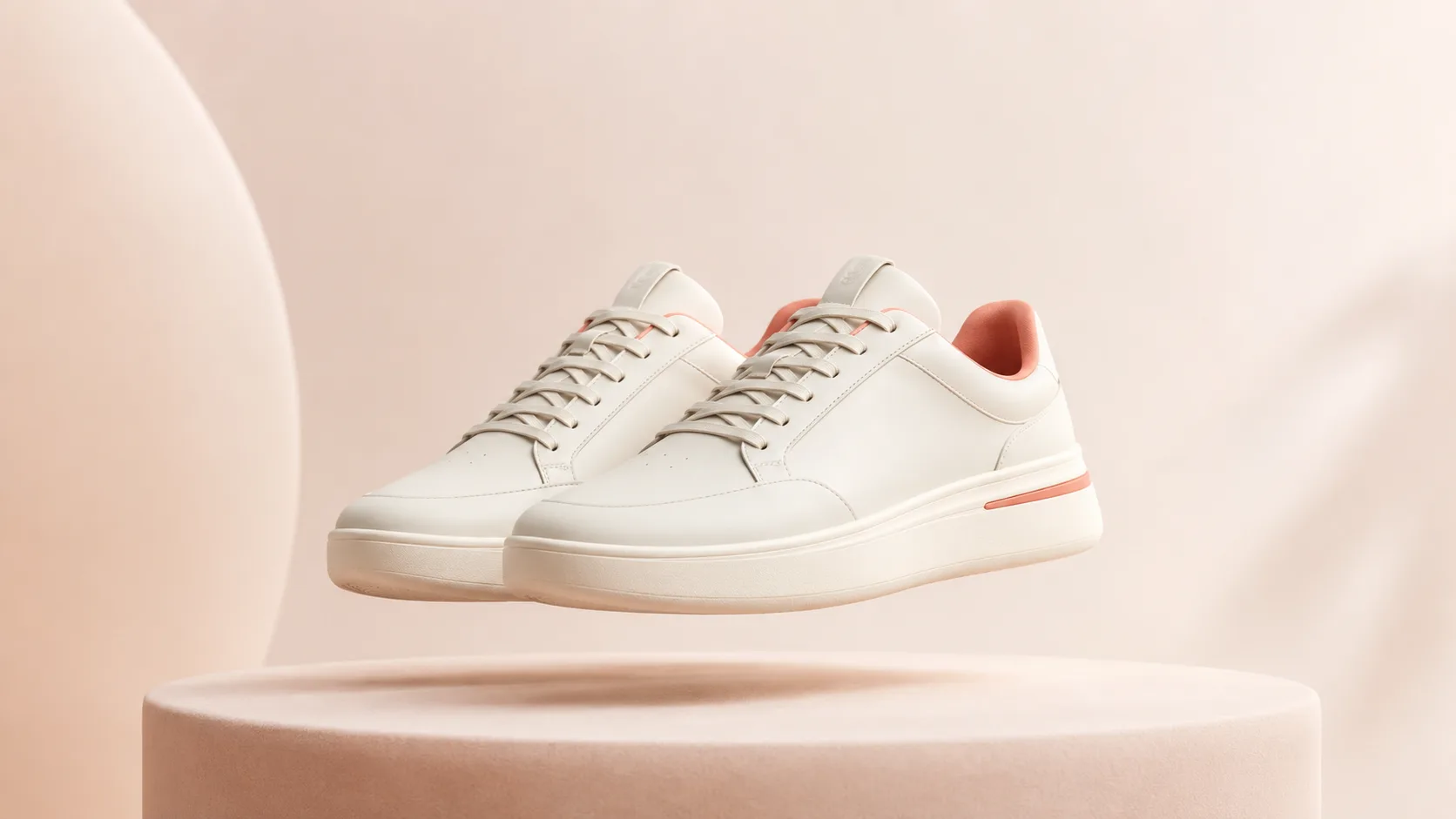 Pair of clean minimalist sneakers floating at an angle above a soft podium