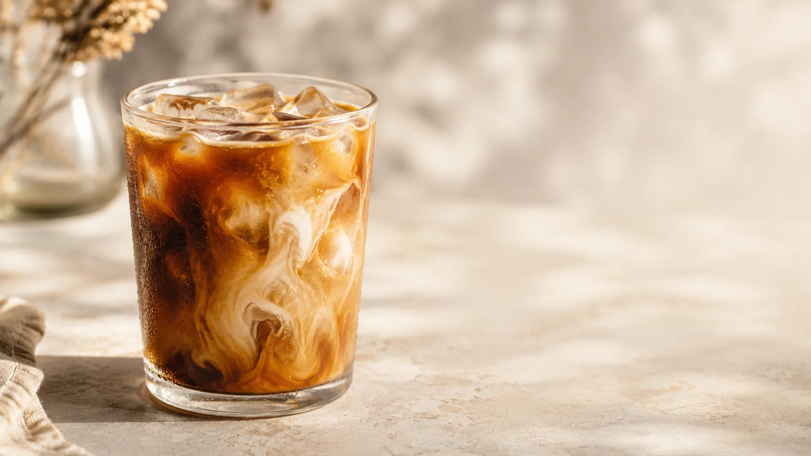 Editorial photograph of a glass of iced coffee with a swirl of milk and ice