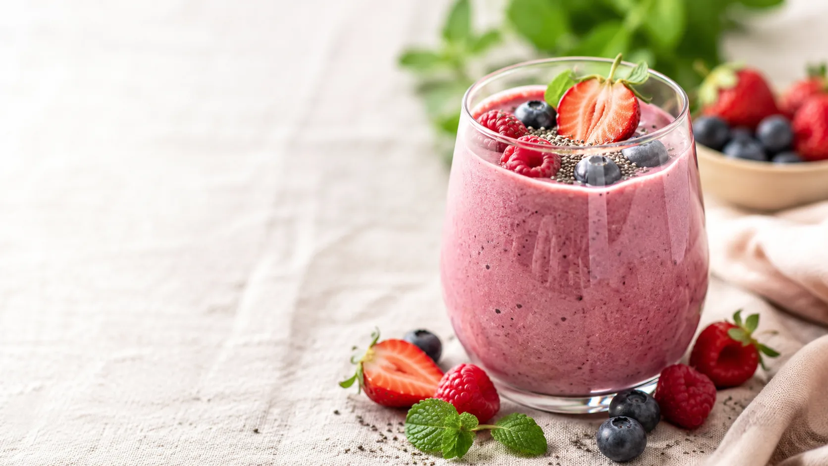 Editorial photograph of a vibrant smoothie topped with fresh fruit and seeds