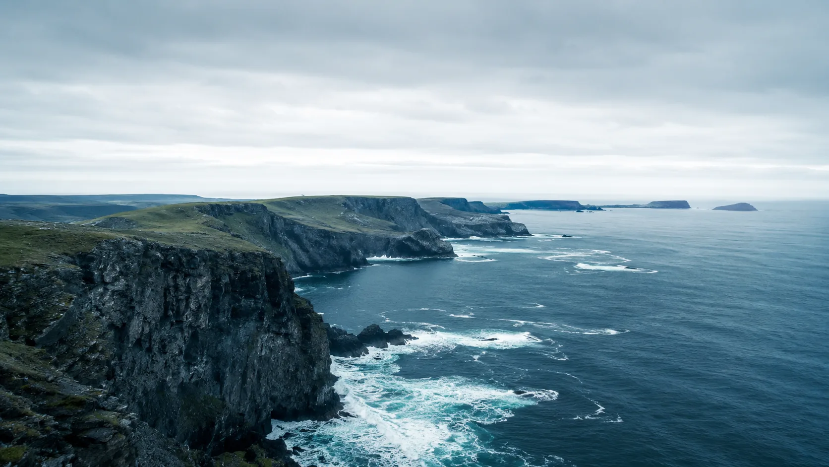 Editorial landscape photograph of dramatic coastal cliffs meeting the ocean with white surf