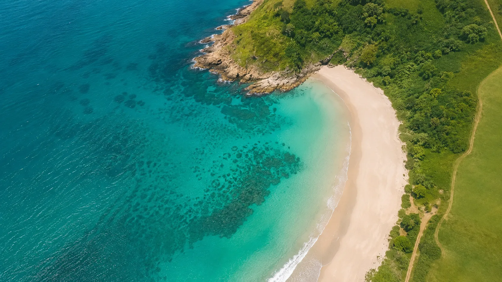 Editorial aerial photograph of a curving coastline with turquoise shallows and pale sand