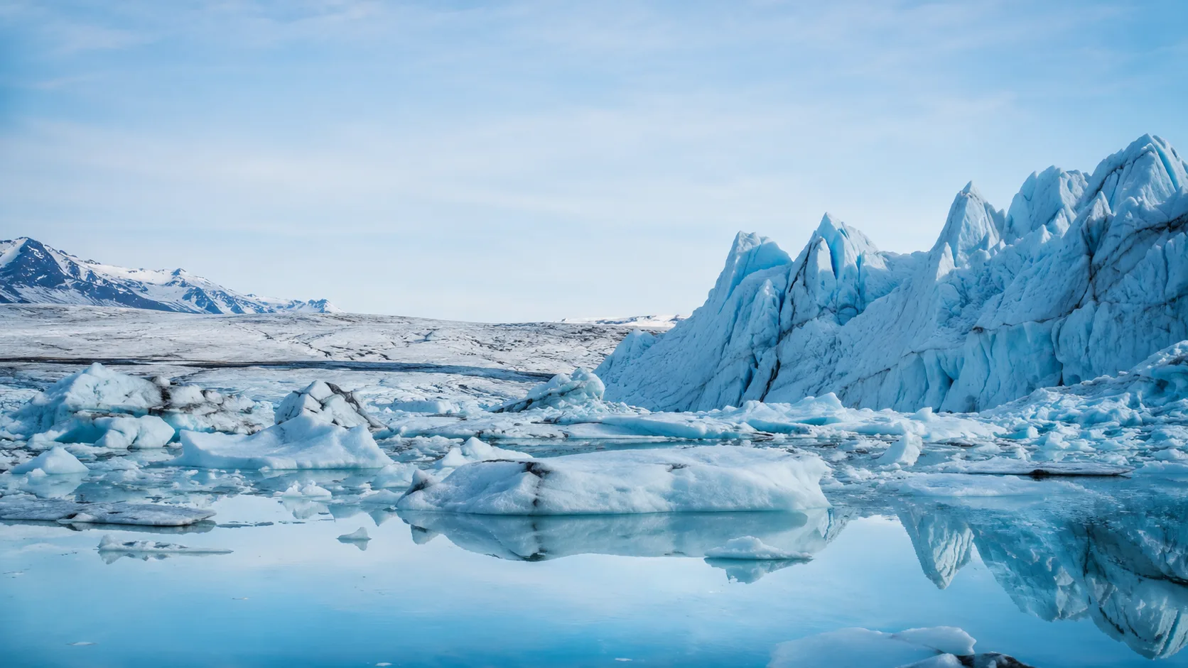 Editorial landscape photograph of a glacier landscape with pale blue ice and a meltwater lagoon