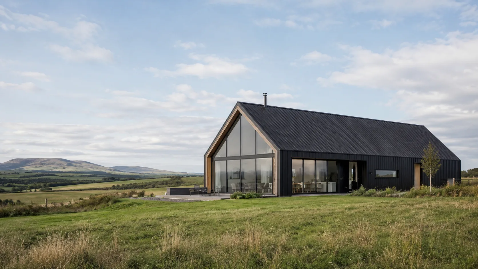 Editorial architecture photograph of a modern barn-style house in dark cladding in open countryside