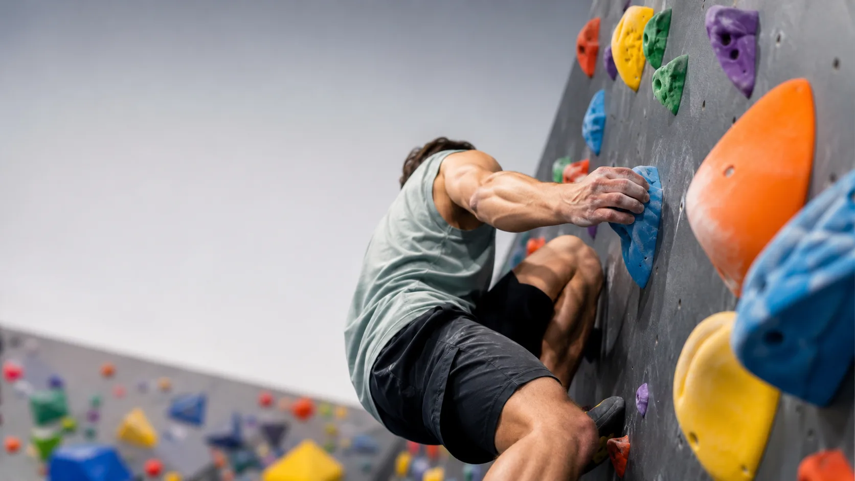 Editorial sports photograph of an indoor climber mid-move on a bouldering wall