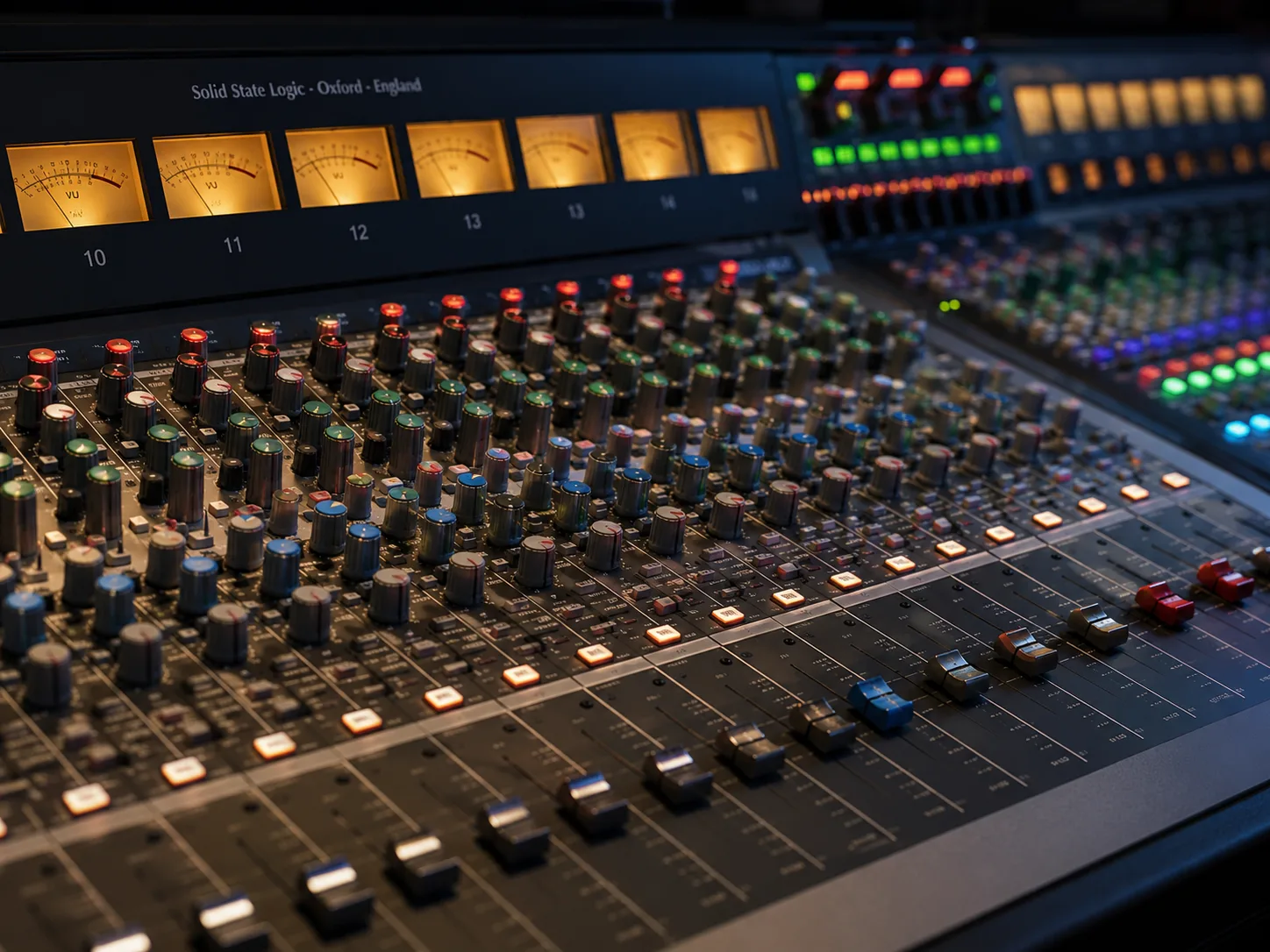 Editorial music macro of a mixing console with backlit faders, glowing VU meters and rows of color-coded knobs at shallow depth of field